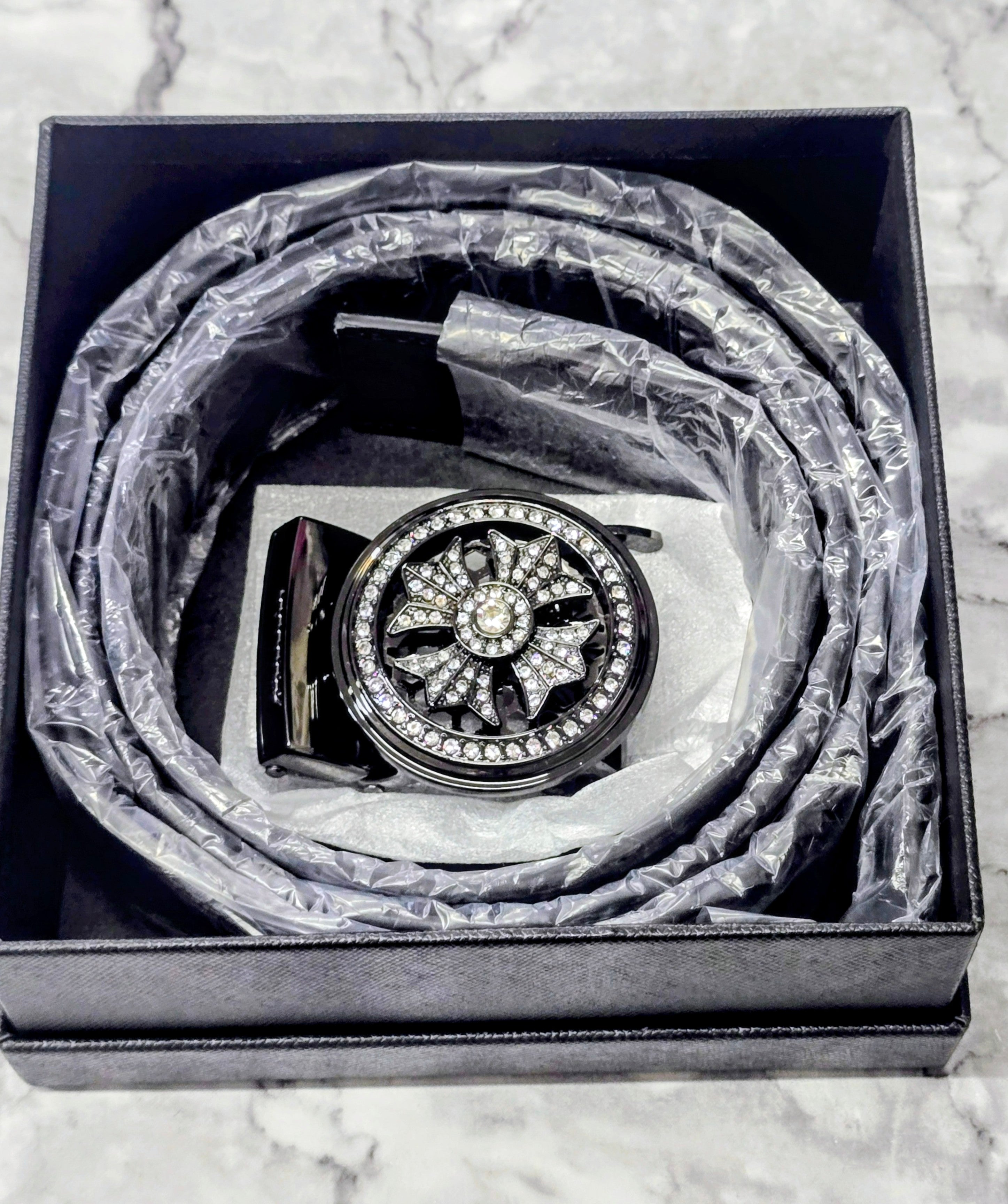 Men's black belt with ornate round rhinestone buckle, coiled in box