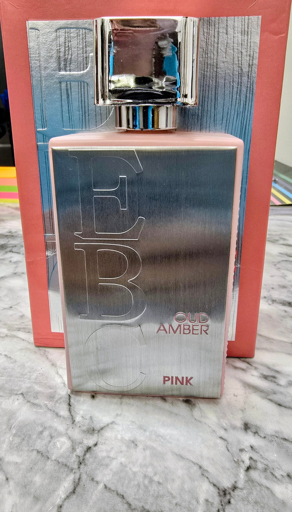 Unisex perfume bottle with silver-blue gradient, pink tint, and chrome cap.